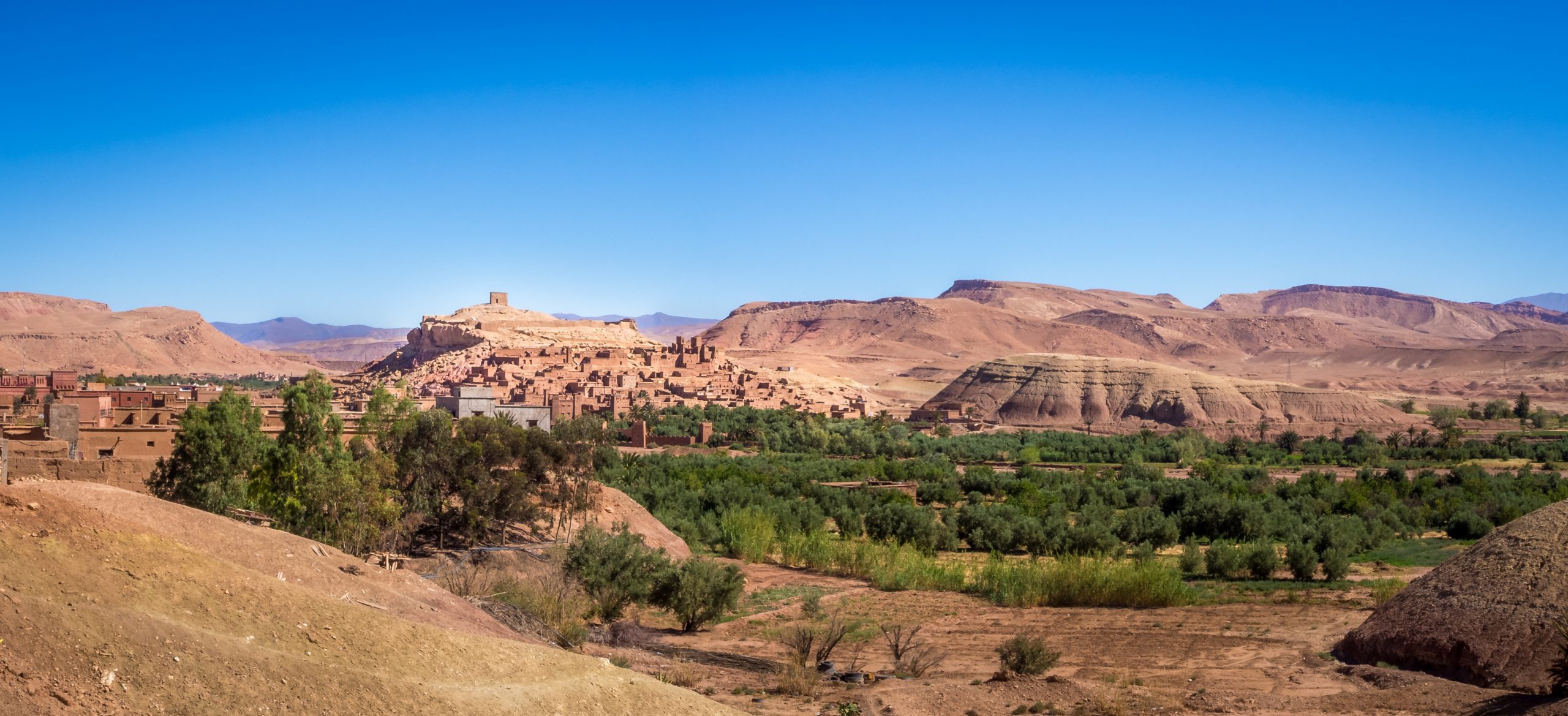 The Ksar of Ait-Ben-Haddou surrounded by greenery under the sunlight and a blue sky in Morocco